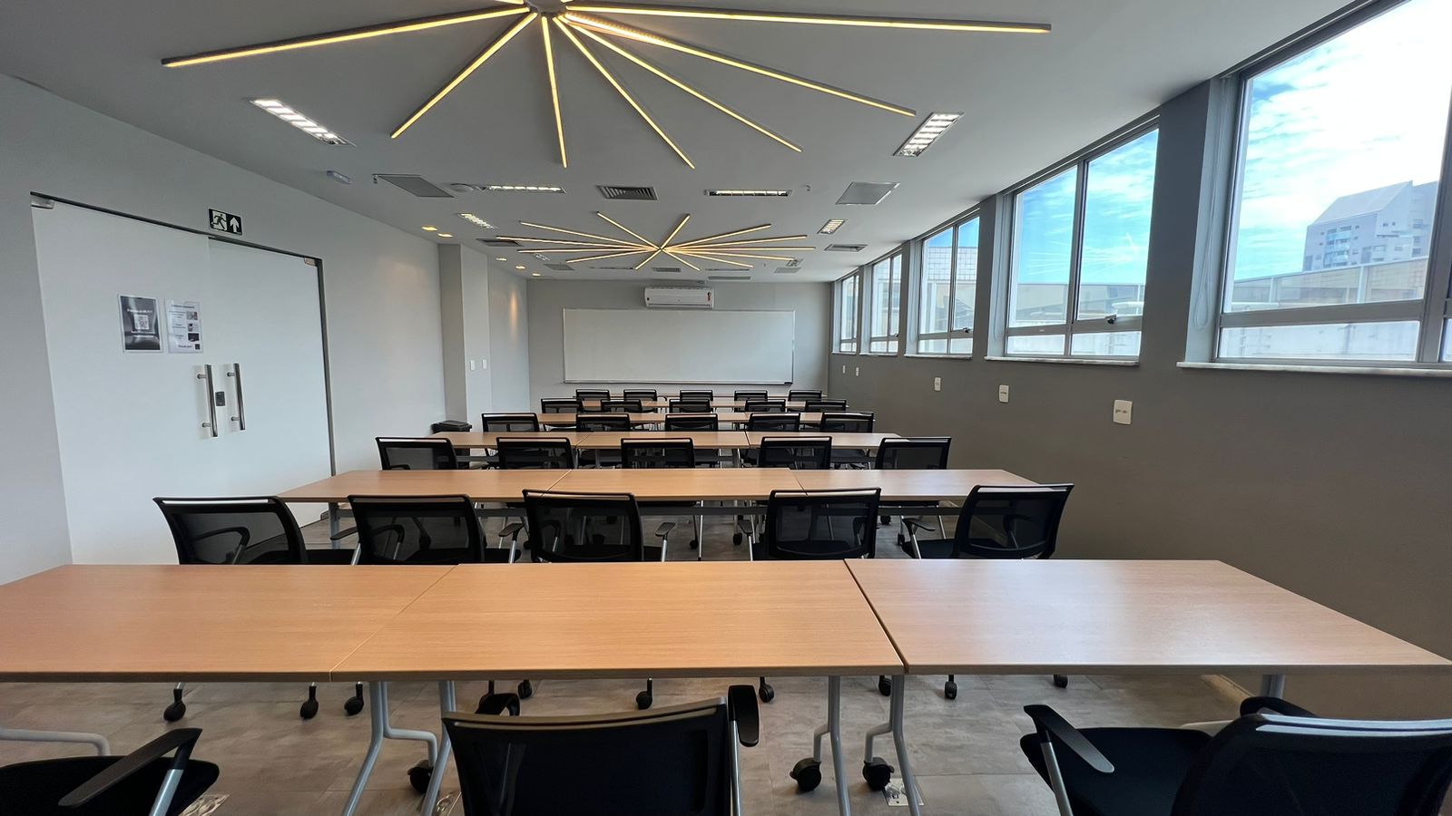 Sala de treinamento vista da entrada, com quadro branco e janelas amplas