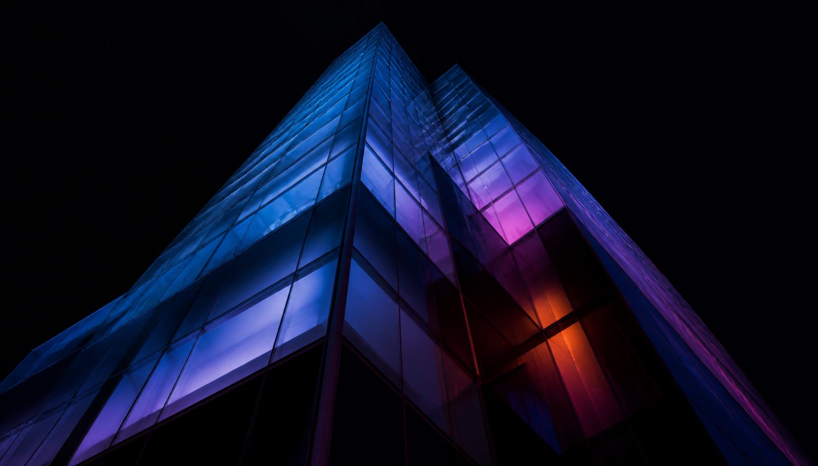 Torre de vidro iluminada por luzes azuis, roxas e magenta à noite